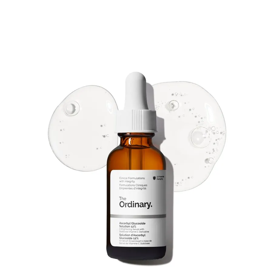 Close-up of The Ordinary Ascorbyl Glucoside Solution 12% bottle held in a hand near a bathroom mirror